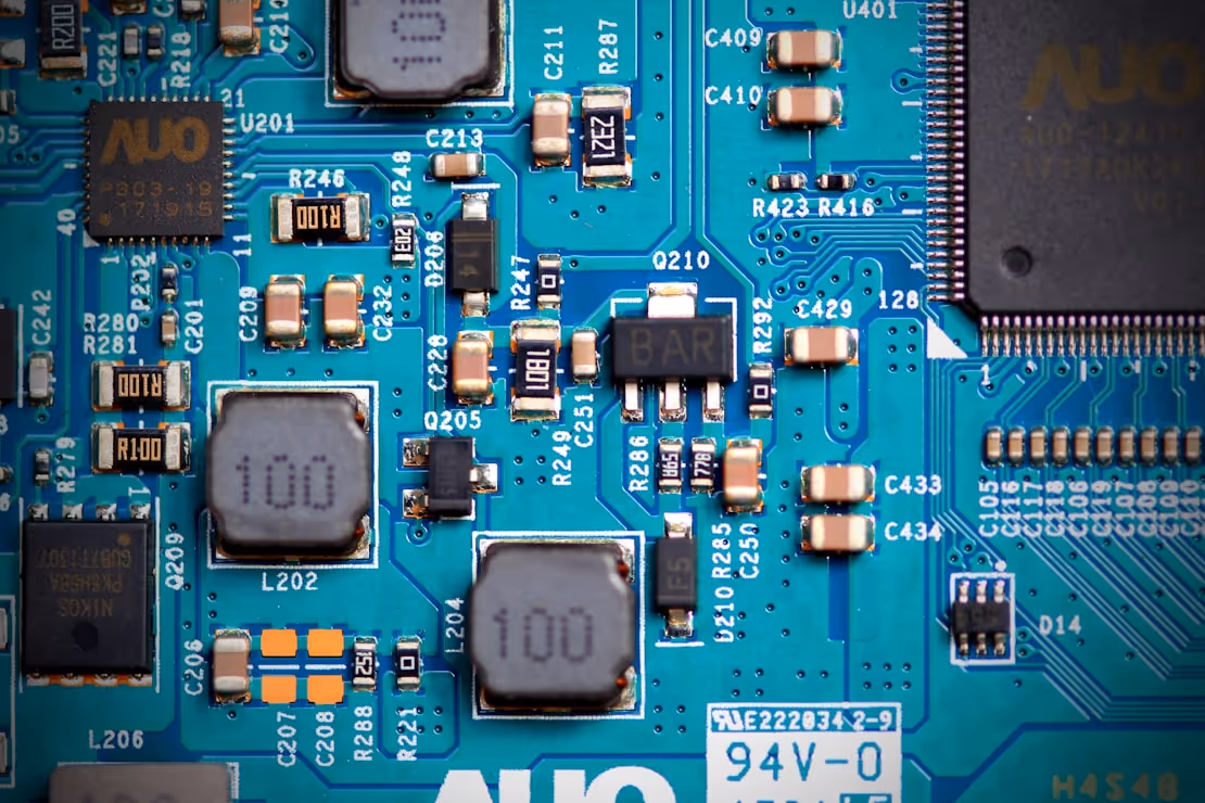 Close-up of a blue printed circuit board with black and beige electronic components, resistors, capacitors, and integrated circuits.